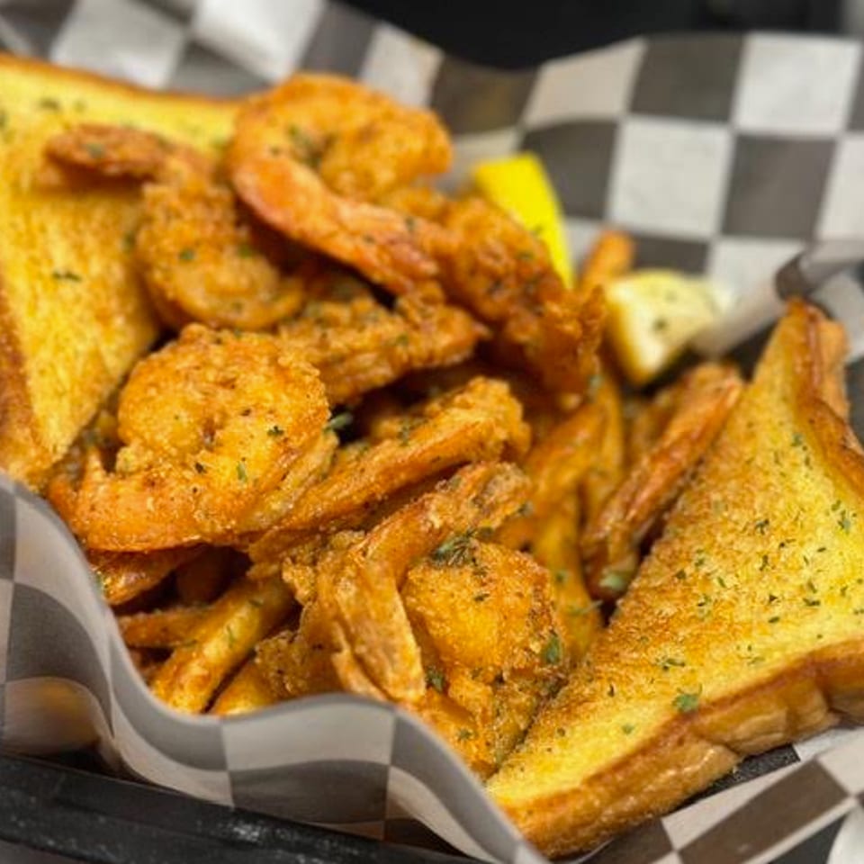 Crispy fried shrimp and golden french fries served with garlic toast and lemon wedges in a checkered basket.