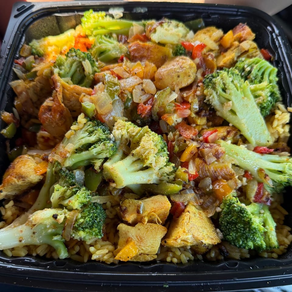 Chicken and broccoli stir-fry with rice, bell peppers, and onions in a black takeout container.