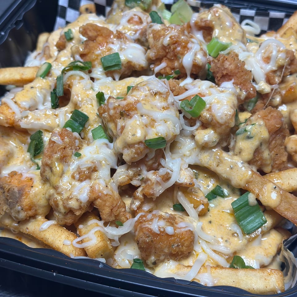 Crispy fries topped with fried shrimp, melted cheese, and green onions in a black container.